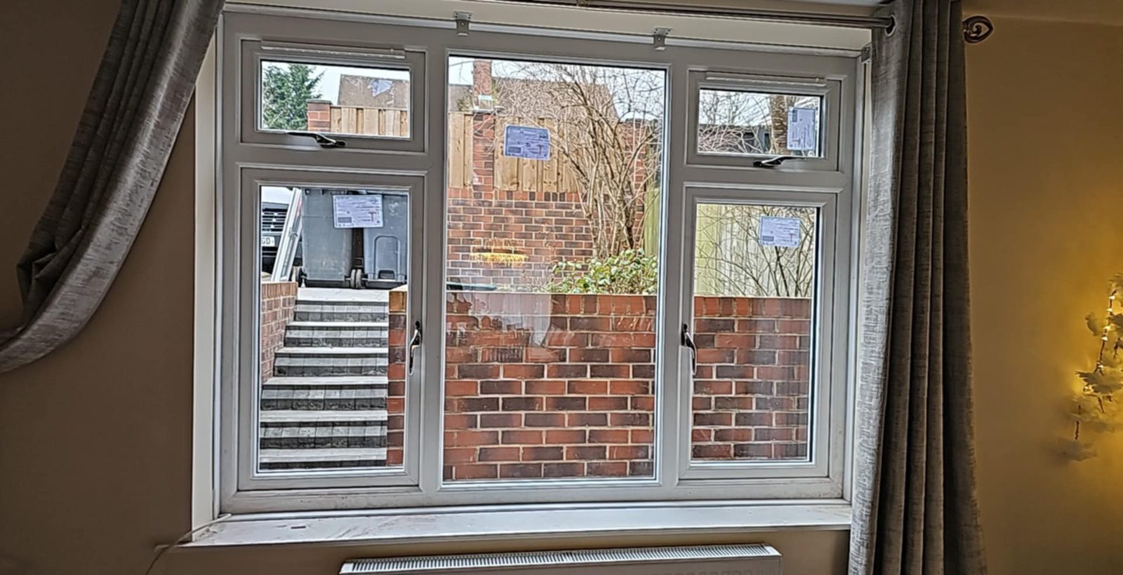 New white uPVC window with top openers, fitted in a living room and looking out over a back yard